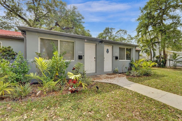 view of front of property with stucco siding, a front lawn, and fence