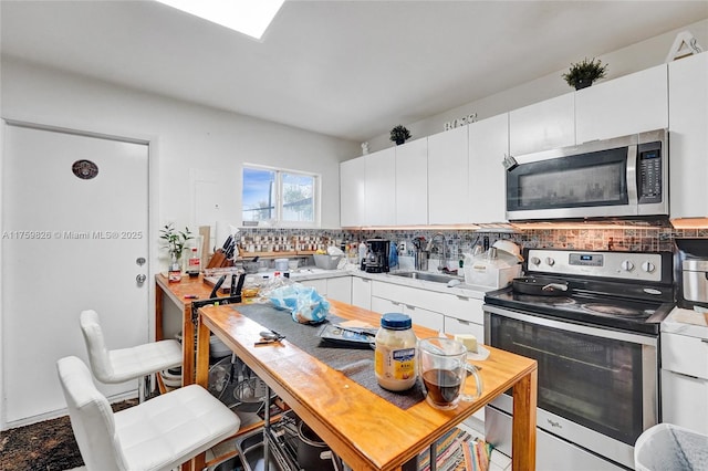 kitchen with a sink, decorative backsplash, light countertops, stainless steel appliances, and white cabinetry