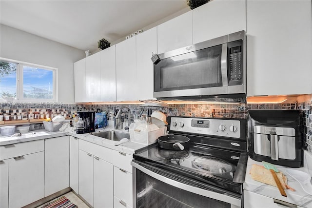 kitchen with light countertops, decorative backsplash, appliances with stainless steel finishes, white cabinetry, and a sink