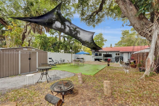 view of yard with a fenced backyard, an outdoor fire pit, a storage shed, an outdoor structure, and a patio area