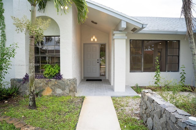 entrance to property with stucco siding and a shingled roof