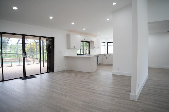 unfurnished living room with light wood-type flooring, lofted ceiling, a sink, recessed lighting, and baseboards