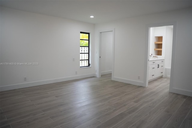 unfurnished bedroom with recessed lighting, baseboards, ensuite bath, and wood finished floors