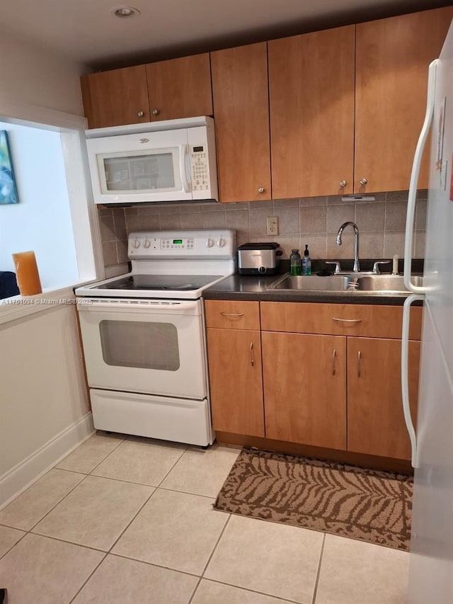 kitchen with dark countertops, light tile patterned floors, decorative backsplash, white appliances, and a sink