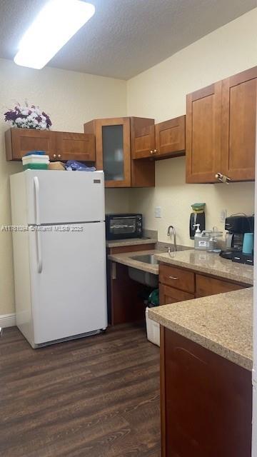 kitchen with brown cabinetry, freestanding refrigerator, dark wood-type flooring, and a sink