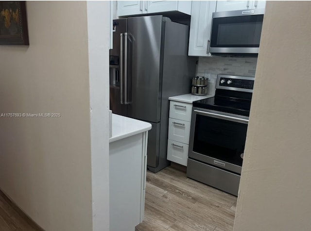 kitchen with white cabinets, stainless steel appliances, light countertops, and light wood-type flooring