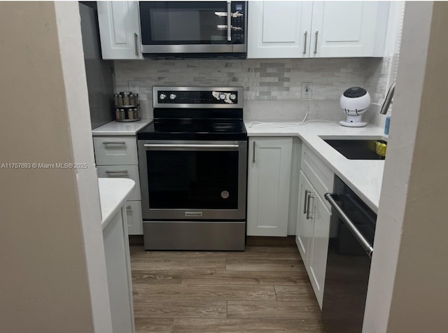 kitchen with backsplash, white cabinets, stainless steel appliances, and wood finished floors