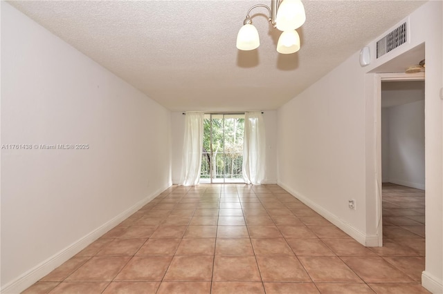 spare room featuring light tile patterned floors, baseboards, visible vents, a textured ceiling, and a notable chandelier