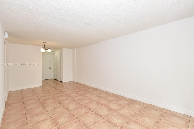 empty room featuring an inviting chandelier, baseboards, and a textured ceiling