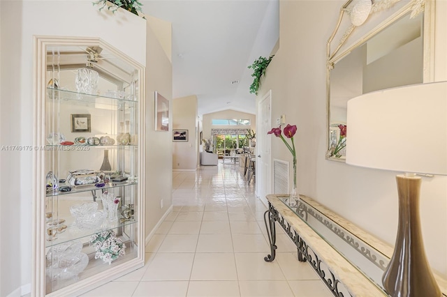 hallway featuring light tile patterned floors, visible vents, baseboards, and lofted ceiling