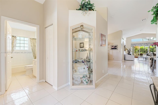 corridor with light tile patterned floors, baseboards, visible vents, and high vaulted ceiling