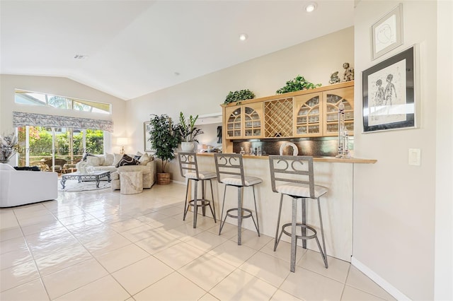 kitchen featuring light tile patterned floors, lofted ceiling, glass insert cabinets, a kitchen breakfast bar, and tasteful backsplash