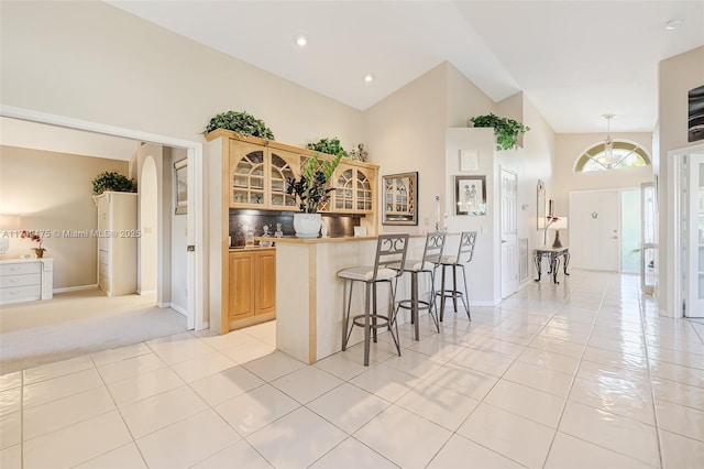 kitchen featuring a breakfast bar, light brown cabinetry, arched walkways, light tile patterned floors, and glass insert cabinets