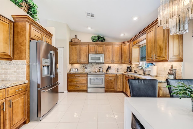 kitchen featuring visible vents, vaulted ceiling, appliances with stainless steel finishes, brown cabinetry, and a sink