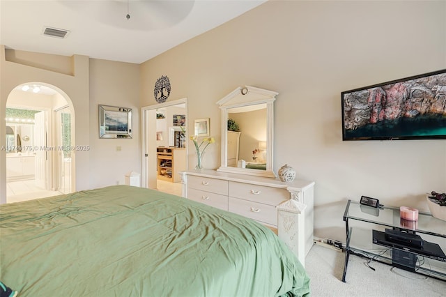 carpeted bedroom with visible vents, arched walkways, and ensuite bath