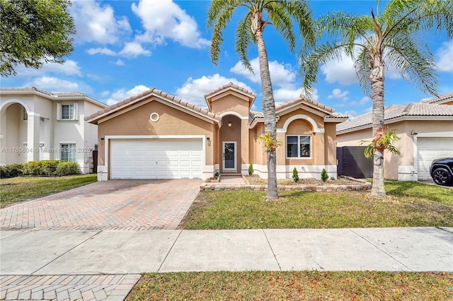 mediterranean / spanish house with stucco siding, an attached garage, decorative driveway, and a front lawn