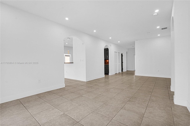 empty room featuring light tile patterned floors, recessed lighting, visible vents, and arched walkways