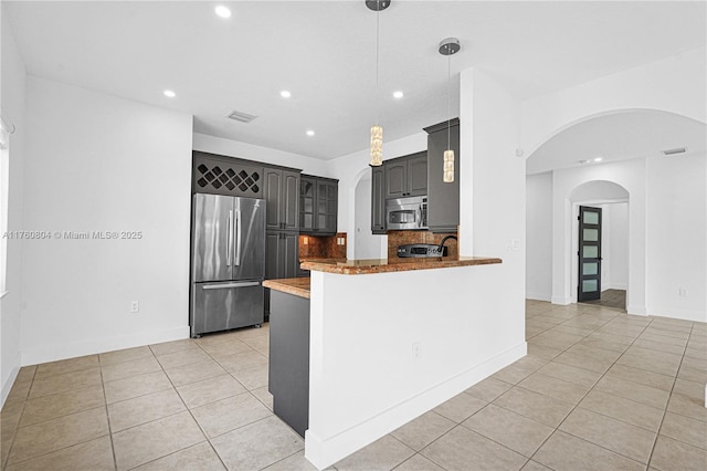 kitchen with backsplash, light tile patterned floors, a peninsula, arched walkways, and stainless steel appliances