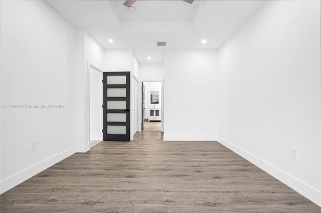 spare room featuring recessed lighting, baseboards, a tray ceiling, and wood finished floors