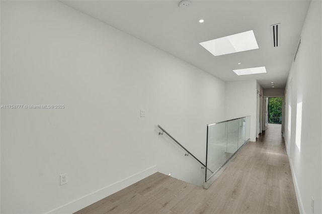 hall with baseboards, a skylight, an upstairs landing, and light wood-type flooring