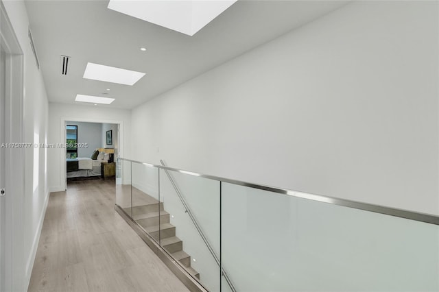 hallway featuring baseboards, visible vents, light wood-type flooring, and a skylight
