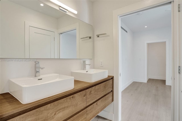 bathroom featuring double vanity, a sink, baseboards, and wood finished floors