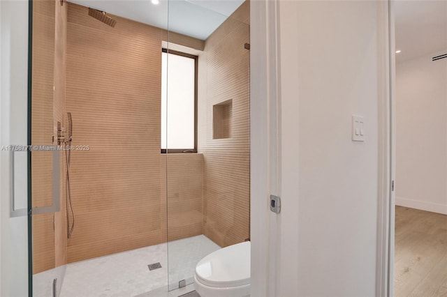 bathroom with baseboards, a tile shower, wood finished floors, and toilet