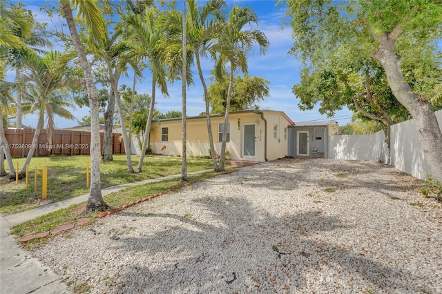 view of front of house with stucco siding, gravel driveway, a front yard, and fence