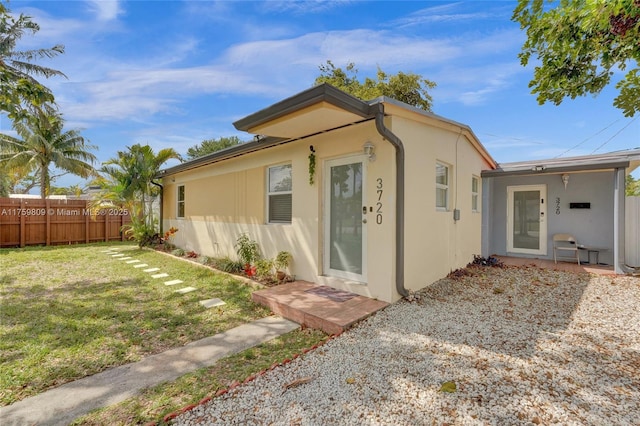 view of front facade featuring stucco siding, a front lawn, and fence