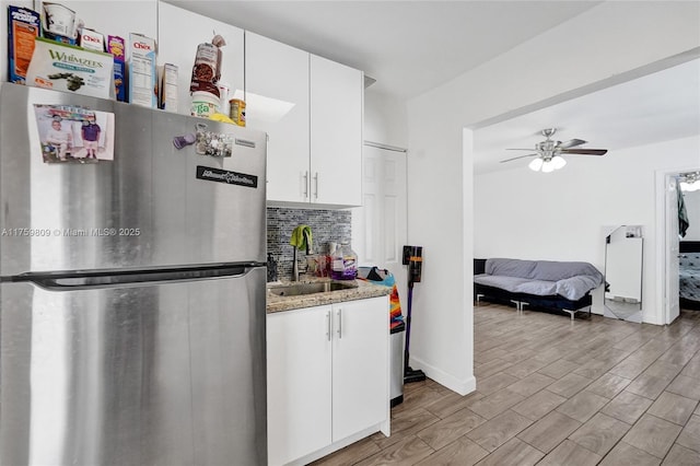 kitchen featuring wood finished floors, freestanding refrigerator, a sink, white cabinetry, and tasteful backsplash