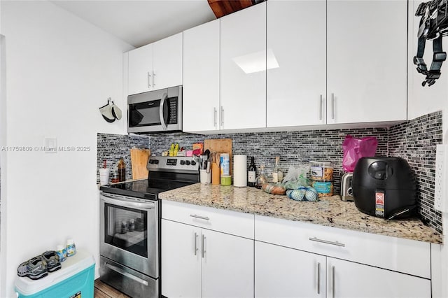 kitchen with white cabinetry, light stone counters, backsplash, and stainless steel appliances