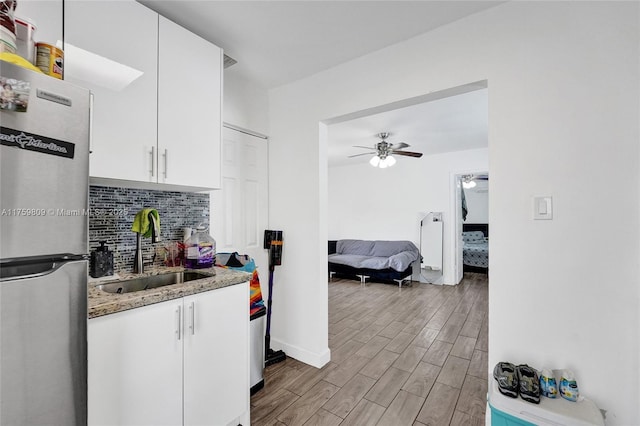 kitchen featuring a ceiling fan, a sink, freestanding refrigerator, light wood-style floors, and decorative backsplash