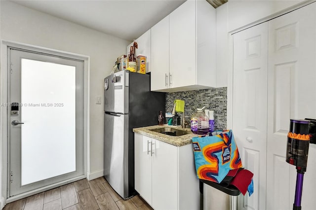 kitchen featuring wood finish floors, freestanding refrigerator, a sink, white cabinets, and backsplash