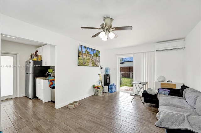 living area with baseboards, a ceiling fan, a wall unit AC, and wood finished floors