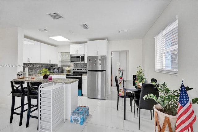 kitchen featuring a kitchen bar, tasteful backsplash, visible vents, and appliances with stainless steel finishes