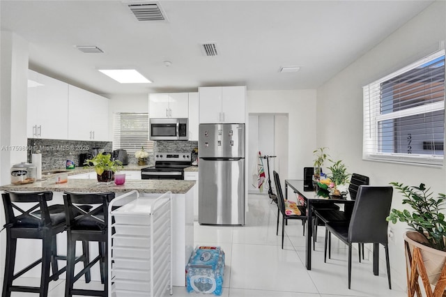 kitchen with visible vents, a kitchen bar, backsplash, and appliances with stainless steel finishes