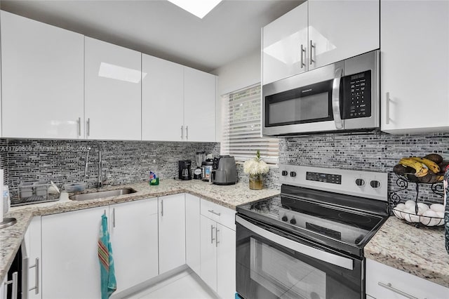 kitchen with tasteful backsplash, light stone countertops, appliances with stainless steel finishes, white cabinetry, and a sink