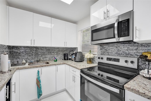 kitchen featuring backsplash, light stone countertops, appliances with stainless steel finishes, white cabinets, and a sink