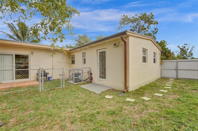 back of house featuring a gate, a yard, and stucco siding