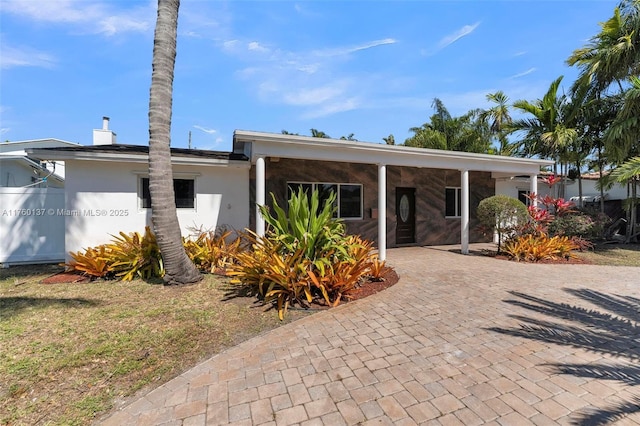 view of front of house with stucco siding, a chimney, and decorative driveway