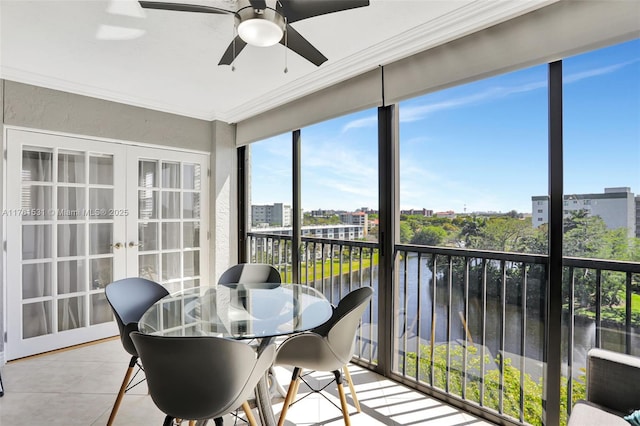 sunroom with french doors, a view of city, ceiling fan, and a water view