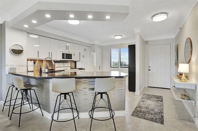 kitchen featuring a kitchen bar, ornamental molding, dark countertops, white appliances, and a peninsula