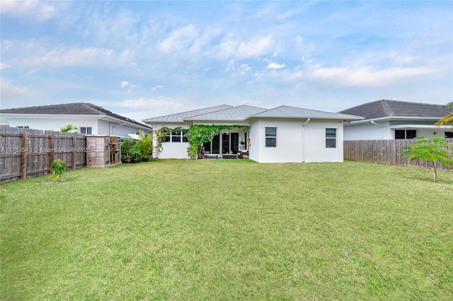 rear view of house featuring metal roof, a lawn, a fenced backyard, and a standing seam roof