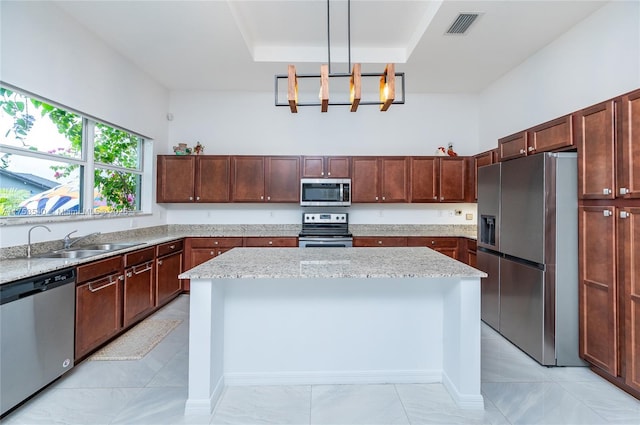 kitchen with visible vents, a sink, a center island, stainless steel appliances, and light stone countertops