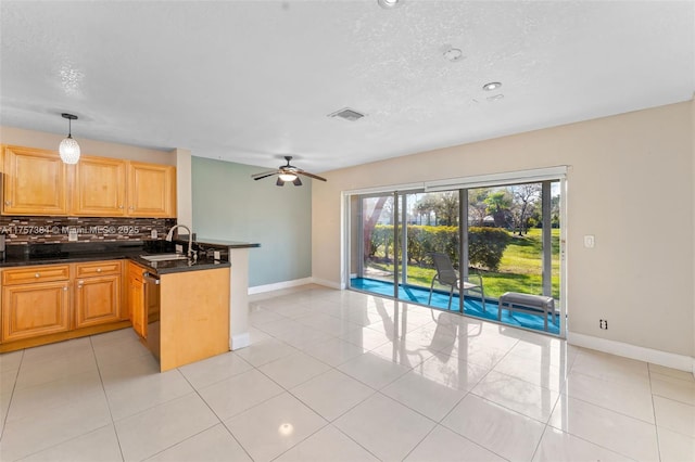 kitchen featuring light tile patterned floors, a peninsula, a sink, dark countertops, and backsplash