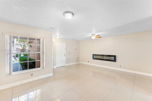 unfurnished living room featuring a ceiling fan, baseboards, visible vents, a textured ceiling, and a glass covered fireplace