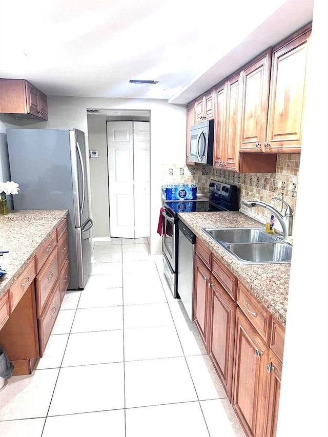 kitchen with a sink, stainless steel appliances, brown cabinetry, light tile patterned floors, and decorative backsplash