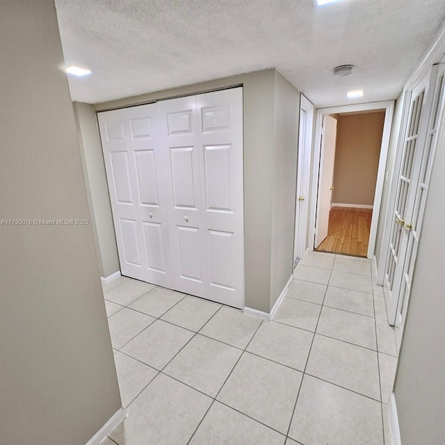 hall featuring light tile patterned floors, baseboards, and a textured ceiling