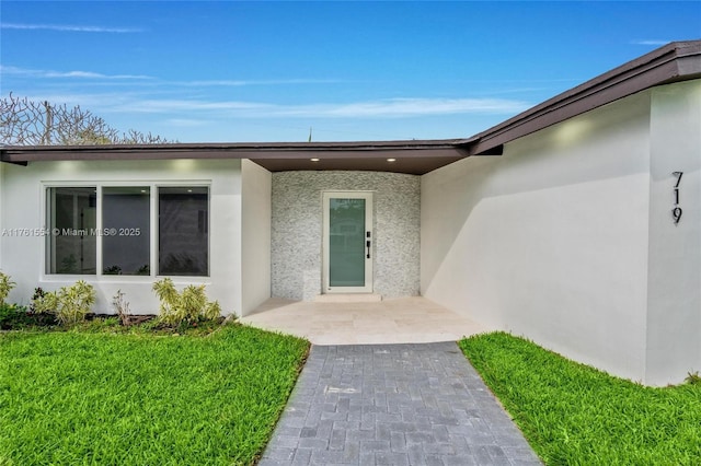 view of exterior entry with stucco siding and a lawn