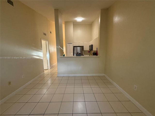 unfurnished living room featuring light tile patterned floors, visible vents, baseboards, and a towering ceiling